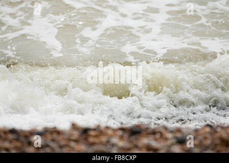 Le onde del mare e la schiuma crash mentre il lavaggio su ghiaia Ciottoli sulla costa britannica beach Foto Stock