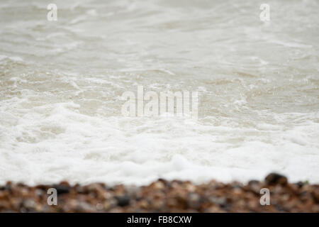 Schiumoso onde del mare lava e si innalza su ciottoli su British costa shingle beach Foto Stock