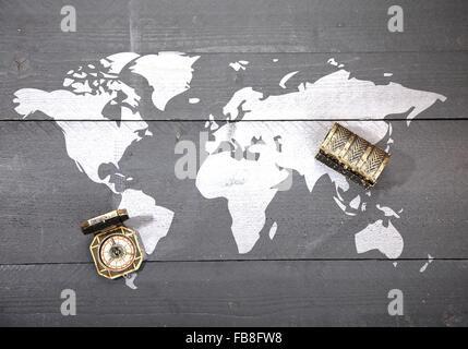 Mappa del mondo con bussola e tesoro su nero scuro dello sfondo in legno Foto Stock