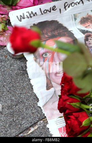 Londra, Gran Bretagna. Xii gen, 2016. Un giornale stampato con la notizia della morte di David Bowie è a sinistra lungo con fiori sul terreno di Brixton, Sud Londra, Gran Bretagna, a gennaio 12, 2016. Credito: Han Yan/Xinhua/Alamy Live News Foto Stock