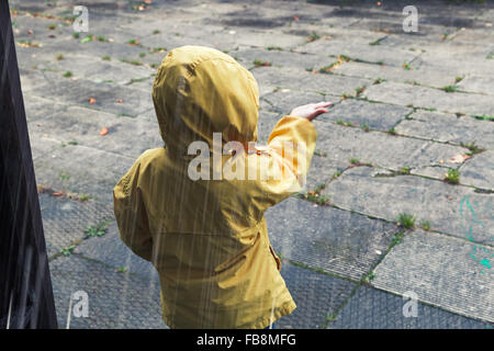 Bambino in giallo impermeabile a giocare con le gocce di pioggia. Vintage correzione tonale foto effetto filtro Foto Stock