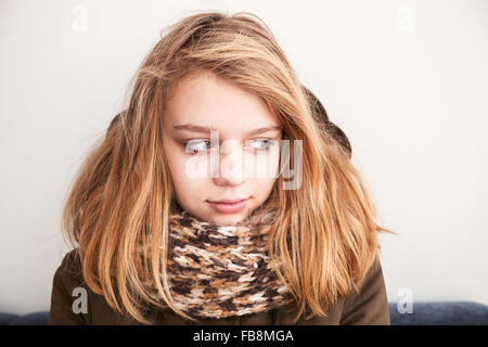 Closeup ritratto della bella bionda caucasica ragazza adolescente in caldi sciarpa oltre il muro bianco sullo sfondo Foto Stock