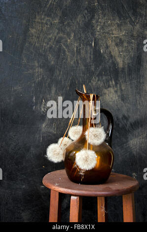 Essiccato tarassaco semi-teste in un vaso su un supporto di legno da rustico sfondo nero Foto Stock