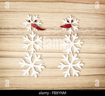 Due pupazzi di neve fatta di fiocchi di neve e peperoncino sullo sfondo di legno. Simbolo dell'inverno. Foto Stock