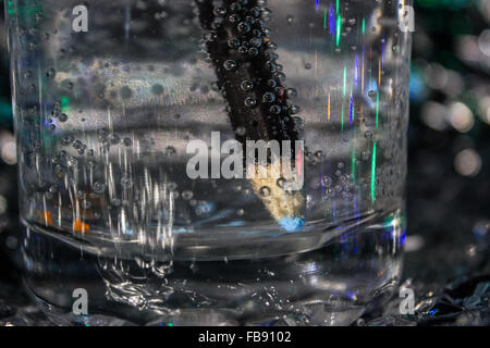 Blu matita acquerello in un bicchiere di acqua frizzante produrre bolle su un foglio di stagno sfondo illuminato con luci fairy. Foto Stock