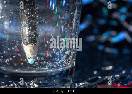 Blu matita acquerello in un bicchiere di acqua frizzante produrre bolle su un foglio di stagno sfondo illuminato con luci fairy. Foto Stock