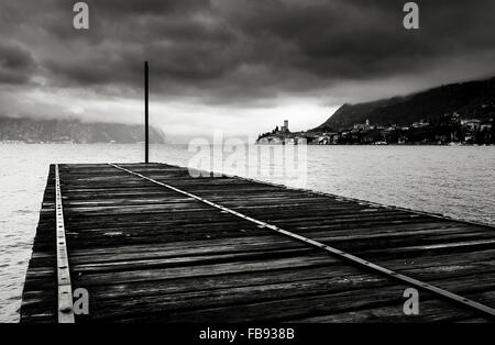 Vista atmosferica di un pontile in legno che si allunga nel Lago di Garda, Italia, con Malcesine in background. Foto Stock
