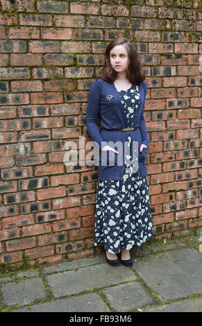 Giovane donna in piedi contro un muro di mattoni vestito in stile anni 1940 Foto Stock