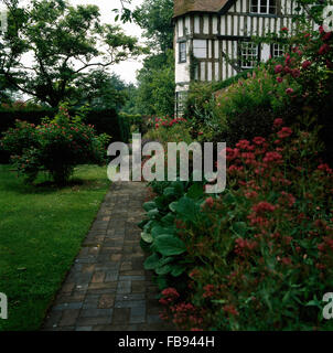 Red Valeriano nel confine accanto al sentiero lastricato nel giardino di nero+con travi di legno bianco country house Foto Stock