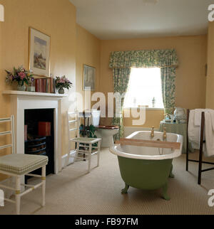 Verde pallido roll top bagno nel paese con bagno floreale verde tende e un tappeto color crema Foto Stock