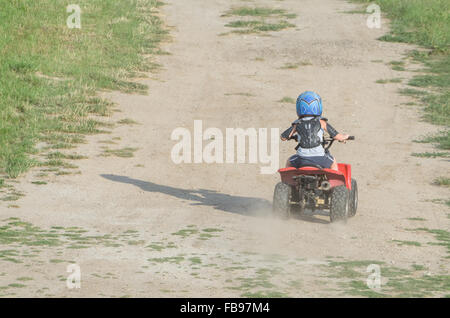 Ragazzo in sella a una Red ATV Quad Bike a secco su un strada sterrata a un giorno di estate Foto Stock