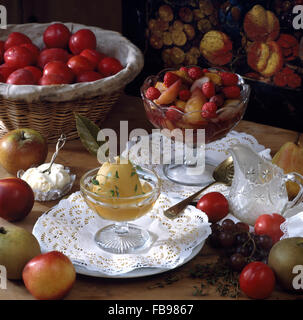 Pera affogata e misto frutta affogato in piatti in vetro sulla tavola con un cesto di prugne fresche Foto Stock