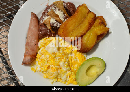 Tipica colazione honduregno di uova strapazzate, plantano fritte, avocado, refried fagioli, tortilla chips e prosciutto Foto Stock