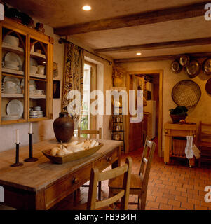 Parte anteriore in vetro armadio sulla parete sopra vintage pine tavolo e sedie in anni ottanta rustica sala da pranzo Foto Stock