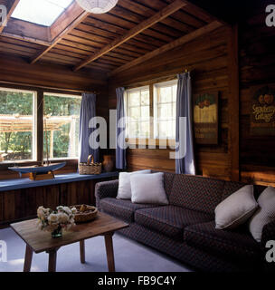 Rivestite di pannelli in legno del soffitto e delle pareti in salotto con un rustico tavolo da caffè in legno e un grigio divano modellato Foto Stock
