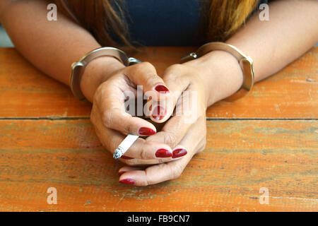 Prigioniero femmina investigato con mani ammanettato e fumare una sigaretta Foto Stock