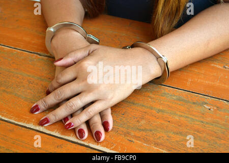 Prigioniero femmina investigato con mani ammanettato su un tavolo Foto Stock