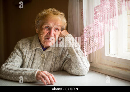 Una donna anziana si siede vicino alla finestra in casa. Foto Stock