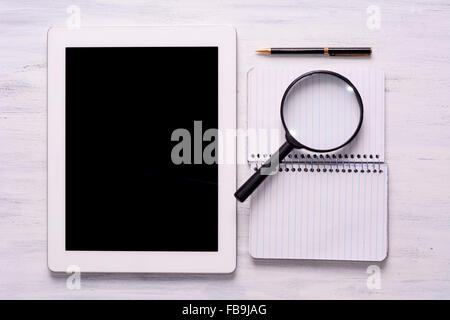 Tablet, notebook, lente di ingrandimento e penna bianca sul tavolo di legno. Vista da sopra con copyspace. Foto Stock