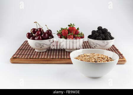 Muesli fatti in casa e le ciliegie e fragole e more in ciotole di ceramica sul tappetino di bambù in background Foto Stock