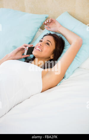 Bella donna avente una telefonata mentre giaceva sul letto Foto Stock