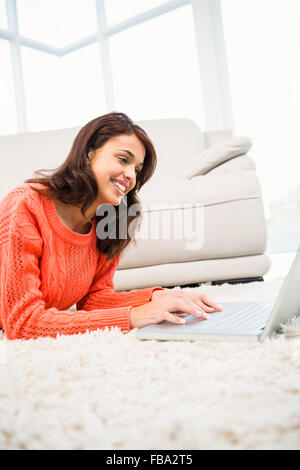 Donna sorridente con notebook mentre sdraiato sul pavimento Foto Stock