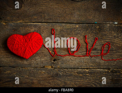 Cuore rosso forma con una iscrizione amore fatti di lana sul vecchio squallido sfondo di legno. Immagine del giorno di San Valentino Foto Stock