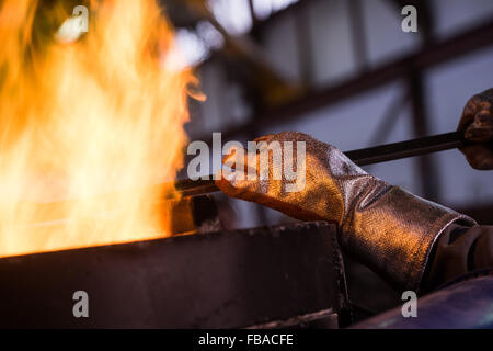 Lavoratore di acciaio in abbigliamento protettivo rastrellatura forno in una fonderia industriale Foto Stock
