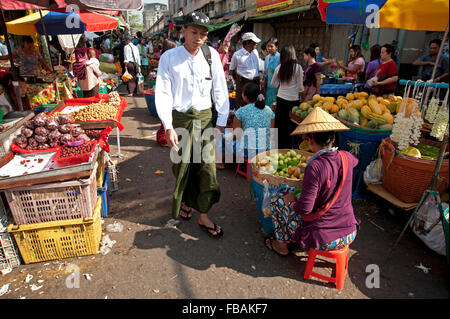 Di birmani uomo vestito nel tradizionale sarong a piedi attraverso un Rangoon street market Myanmar Foto Stock