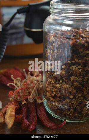 Schiacciato il peperoncino in un vasetto di vetro vicino ad alcuni tutto il peperoncino piccante Foto Stock