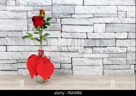 Cuori di San Valentino e rosa rossa in una bottiglia di vetro poste su una squallida scaffale di legno con mensola bianco muro di pietra sullo sfondo Foto Stock