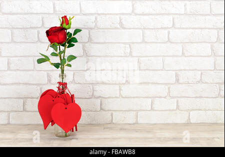 Cuori di San Valentino e rosa rossa in una bottiglia di vetro poste su una squallida scaffale di legno con mattoni bianchi sullo sfondo di parete Foto Stock