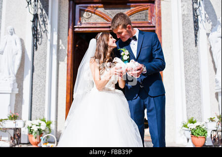 Happy sposi con le colombe a portata di mano la chiesa di sfondo Foto Stock