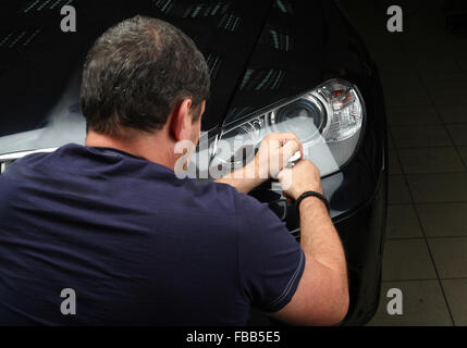 Il lavoratore lucidi ottica dei fari anteriori della macchina con l'attrezzo elettrico. Close up Foto Stock