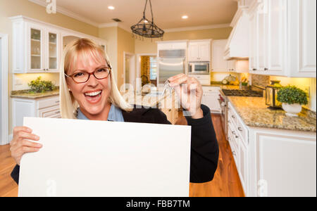 Felice giovane donna tenendo premuto segno di vuoto e le chiavi all'interno della bellissima cucina personalizzata. Foto Stock