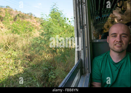 Giovane uomo guarda malati e seccato su un pullman classe di viaggio attraverso la Thailandia Foto Stock