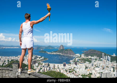 Un vecchio stile atleta in sport bianco uniforme tenendo permanente sport torcia presso skyline della città si affacciano a Rio de Janeiro in Brasile Foto Stock