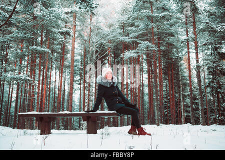 Ragazza slanciata si siede su una panchina in inverno. Foto Stock