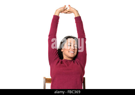 Giovane donna stretching con un sorriso di piacere alzando le braccia sopra la sua testa mentre è seduto in una sedia come lei chiude gli occhi Foto Stock