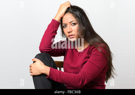 Premuto preoccupato giovane donna seduta che abbraccia il suo ginocchio guardando la telecamera con un grave disperati expression Foto Stock