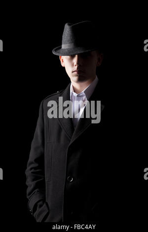 Bello elegante uomo che indossa un cappello e soprabito, raffreddare, pericolose, misterioso straniero, metà illuminata nel buio Foto Stock