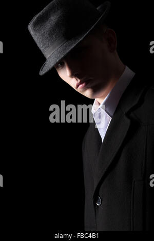 Bello brutale cerca uomo in cappotto e hat nelle tenebre, studio shot su sfondo nero, bassa illuminazione tasto Foto Stock