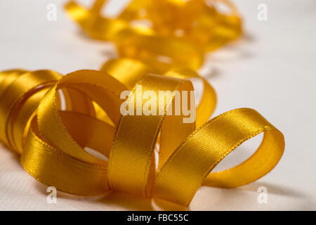 Close-up di golden ribbon unraveling in un pasticcio su sfondo bianco Foto Stock