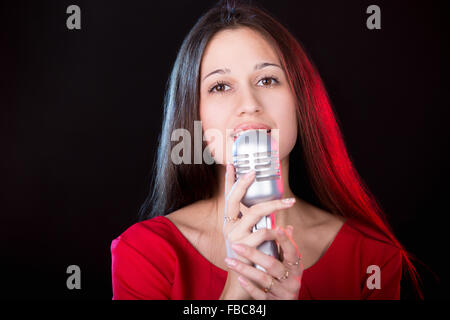 Ritratto di bella ragazza emotiva cantante in abito rosso cantando holding argento microfono vintage Foto Stock