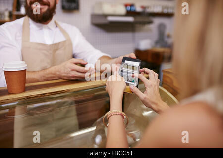 Giovane donna di pagare per un caffè con carta di credito presso la caffetteria. Focus sulla donna mani immettendo il PIN di sicurezza in un lettore di carte di credito. Foto Stock