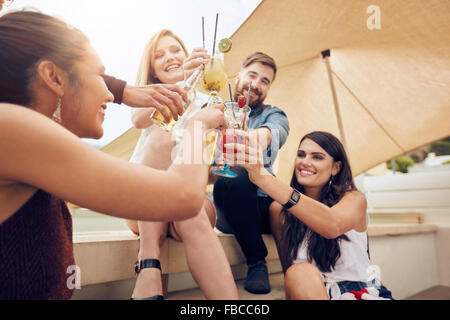 Un gruppo di giovani felici hanno il tifo con cocktail e sorridere mentre festeggiare insieme sul tetto. Multirazziale giovani amici ha Foto Stock