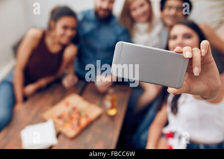 I giovani in una parte contraente di adottare qualsiasi ritratto di auto con il telefono cellulare. Focus su smart phone nella donna la mano. Un gruppo di giovani sitt Foto Stock