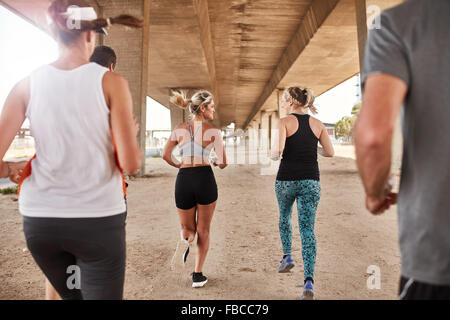 Ritratto di gruppo di corridori in abbigliamento fitness in esecuzione sotto un ponte. Giovani uomini e donne in esecuzione insieme. Foto Stock