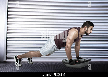 Immagine composita di uomo muscolare facendo bosu ups push Foto Stock