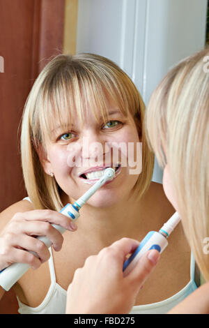 Donna spazzolare i denti vicino a specchio Foto Stock